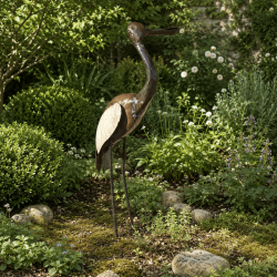Kranich-Gartendekoration zwischen Pflanzen und Natursteinen
