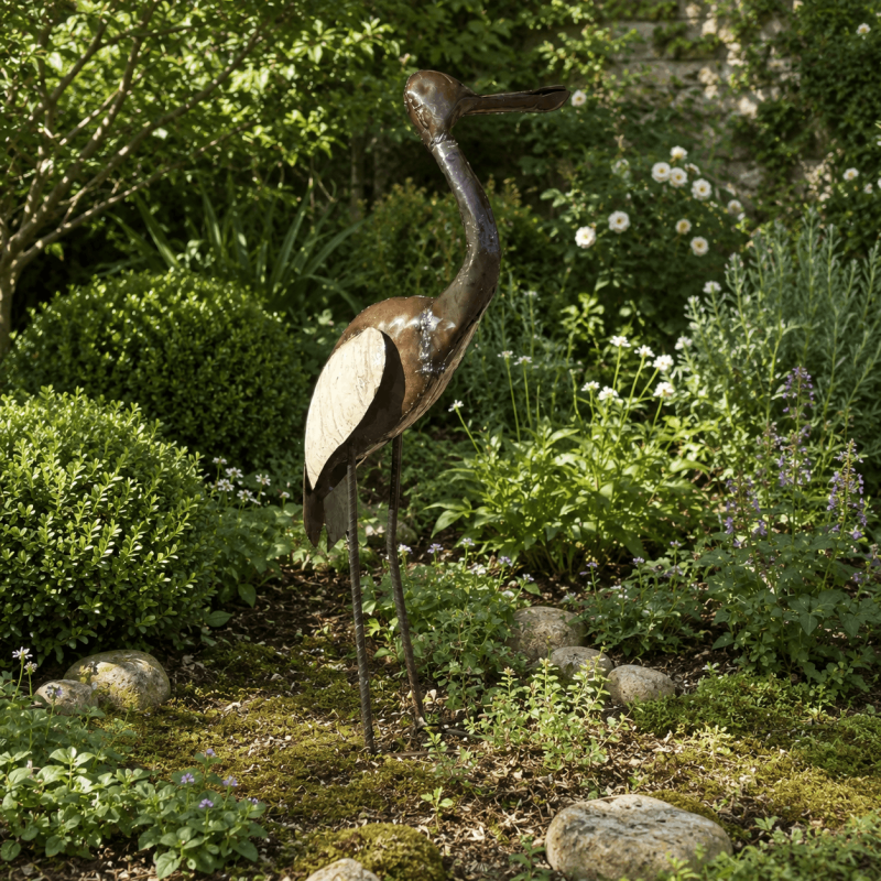 Kranich-Gartendekoration zwischen Pflanzen und Natursteinen