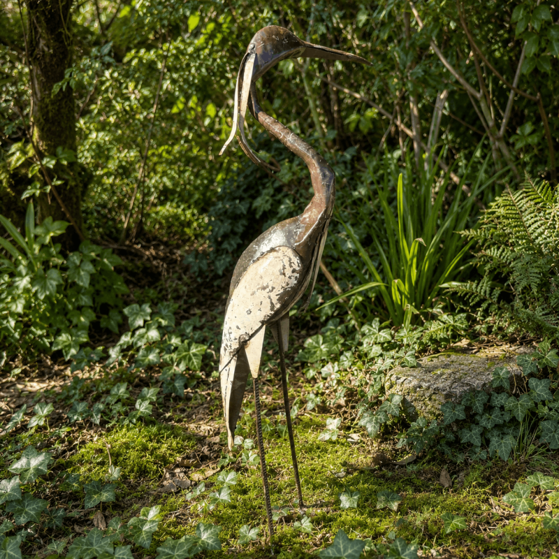 Gartenfigur Reiher zwischen Farnen und Pflanzen